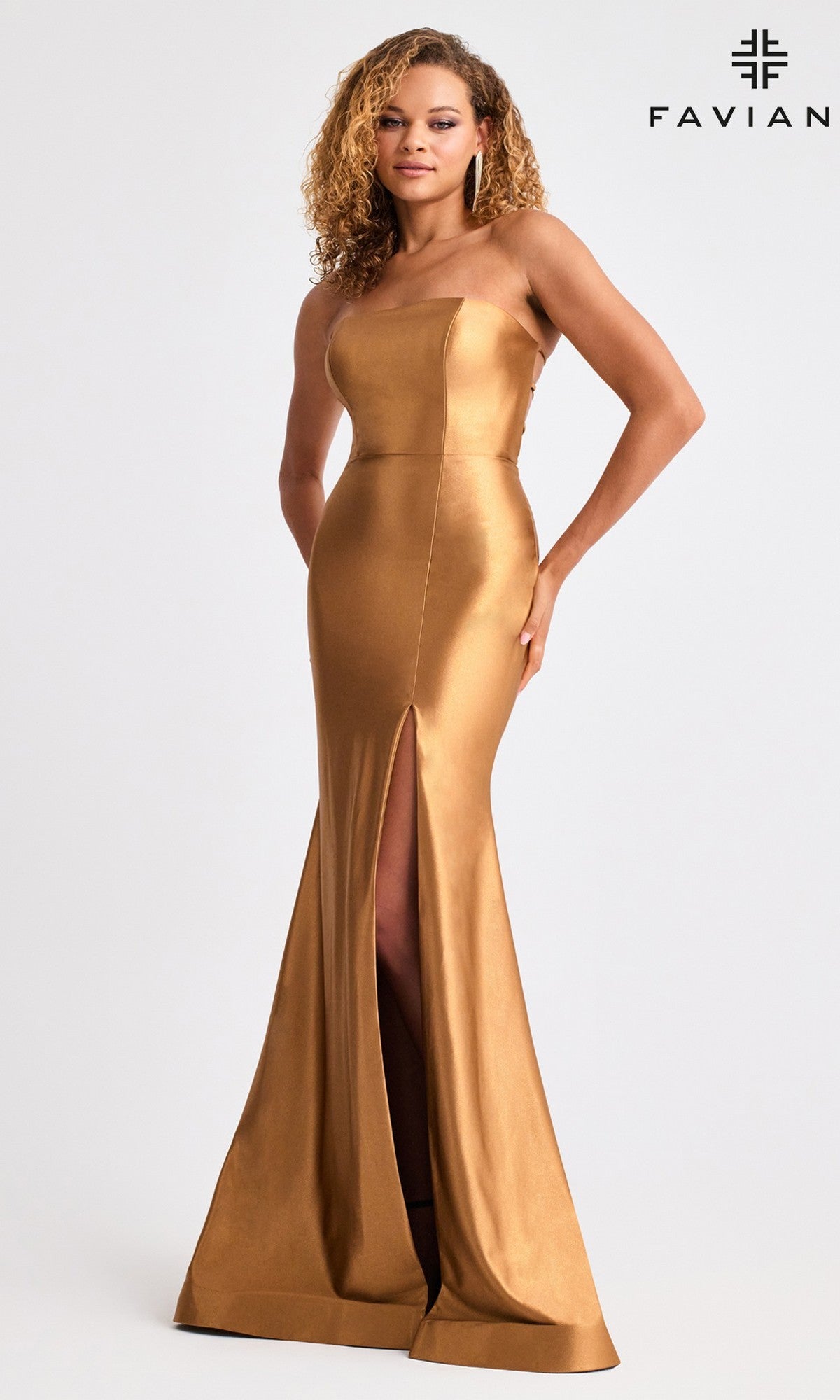 A woman wears the Faviana 11211 Lace-Up Strapless Long Prom Dress, featuring a fitted gold design with a thigh-high slit, ideal for formal occasions. The background is plain with the Faviana logo in the top right corner.